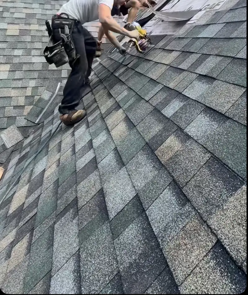 Roofer nailing asphalt shingles with a pneumatic nailer on a sloped roof