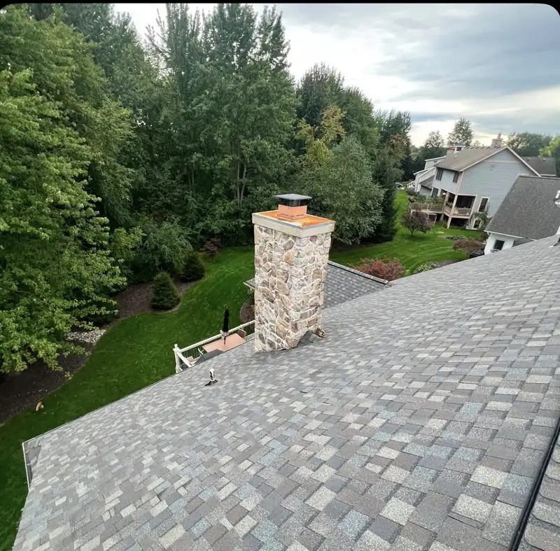 New asphalt shingles and flashing around a stone chimney with a copper cap