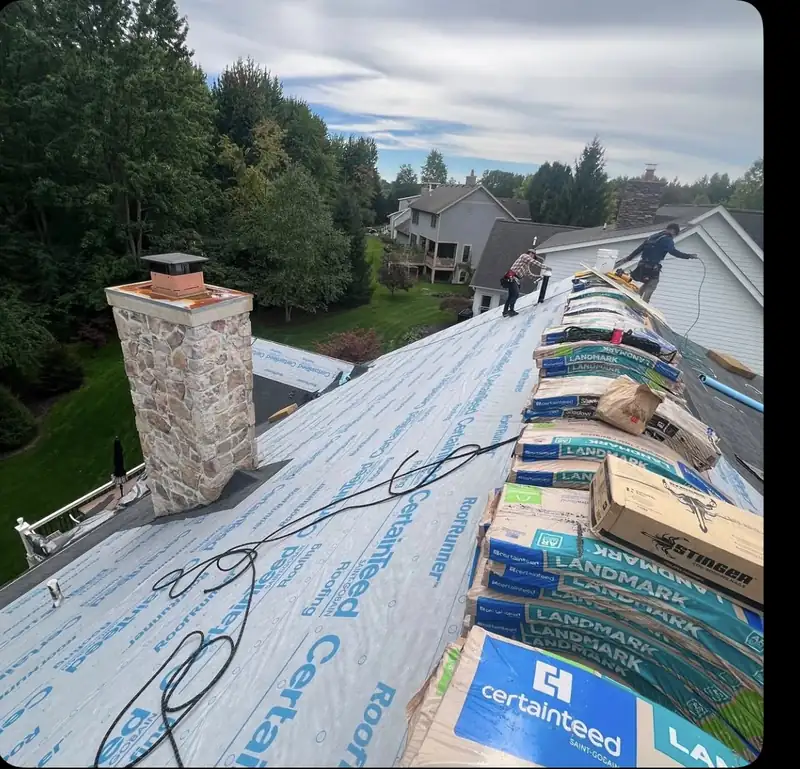 Synthetic roof underlayment installed beside a chimney with shingle bundles stacked on the ridge